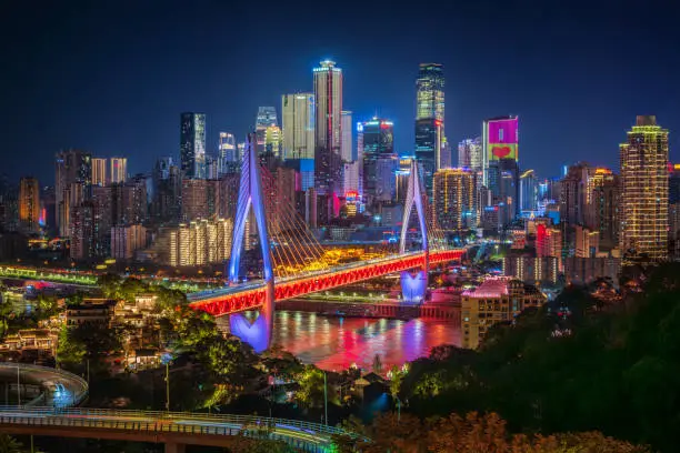 El perfil de rascacielos de Chongqing iluminado de noche, con un puente sobre el río