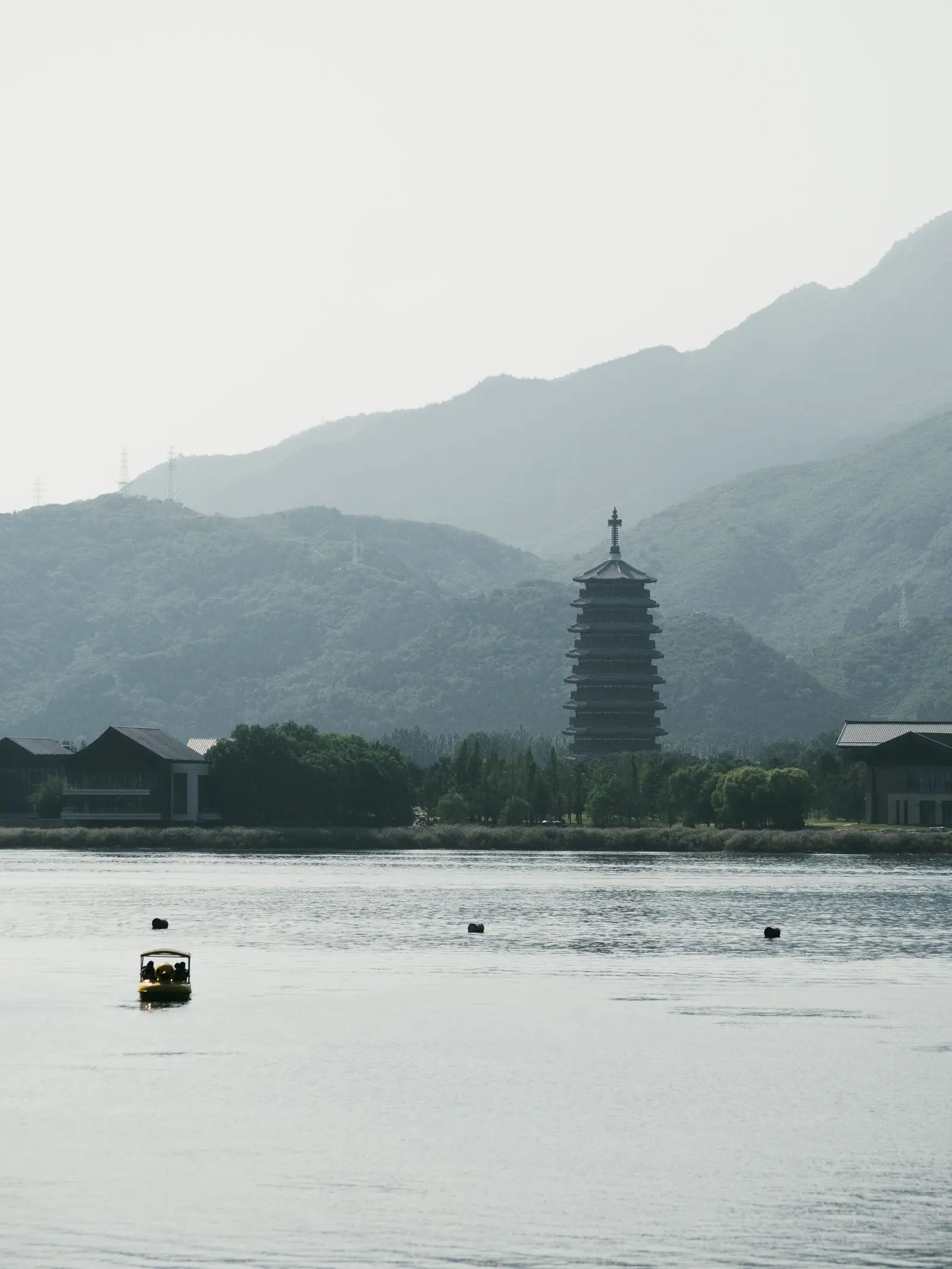 Lago sereno con una pagoda entre montañas brumosas y una pequeña barca