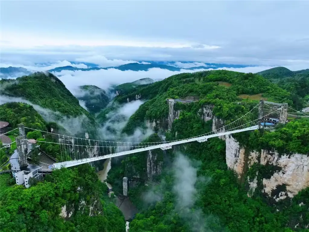 Puente de cristal suspendido sobre el Gran Cañón de Zhangjiajie entre montañas y nubes